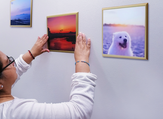 woman with glasses hanging up her gold-framed photo tile